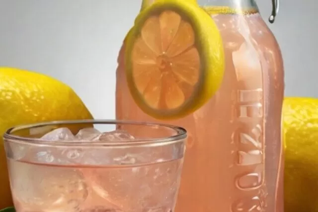 Bebida isotônica caseira de limão em um copo claro, cercada por limões frescos, um pote de mel e uma pitada de sal rosa do Himalaia.