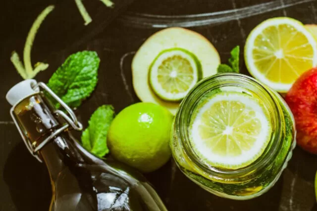 Copo de Kombucha espumante cercado por frutas frescas e ervas.