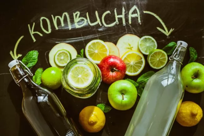 Copo de Kombucha espumante cercado por frutas frescas e ervas.